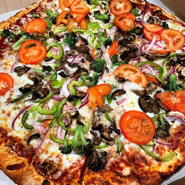 A close-up of a Wasatch Pizza veggie pizza, topped with tomatoes, green peppers, onions, mushrooms, and broccoli.